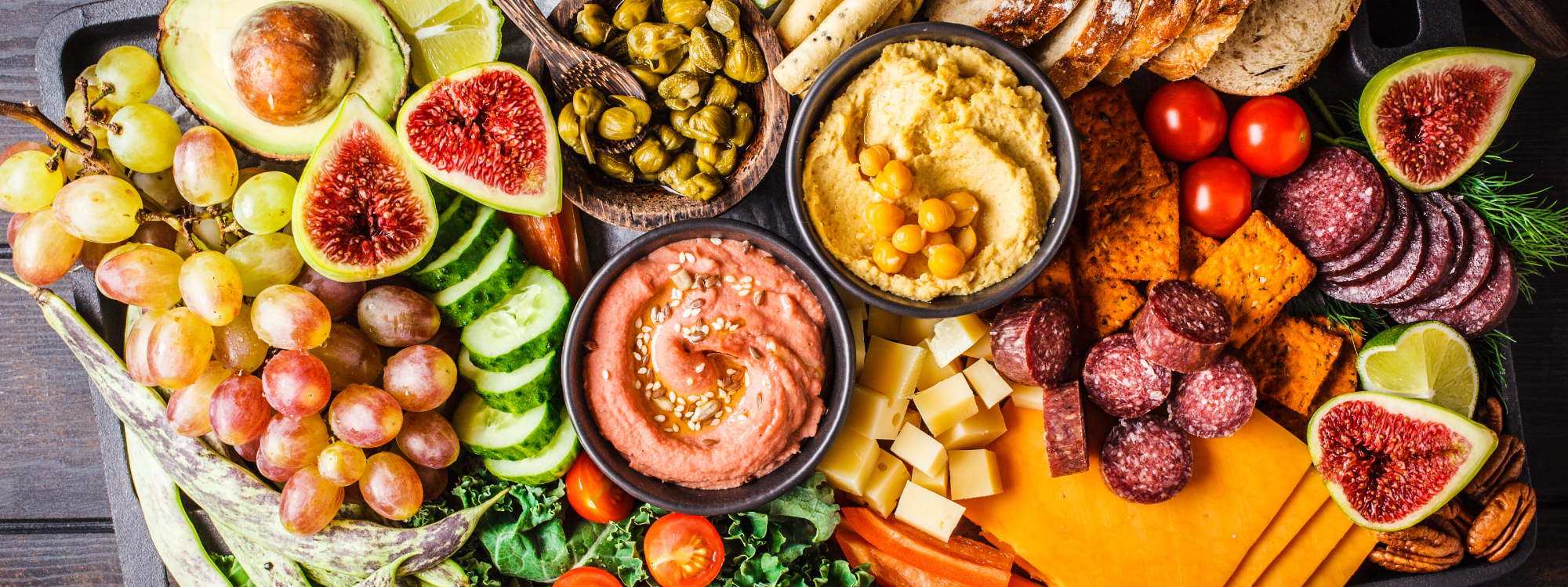 Colorful closeup of a large charcuterie board loaded with various fruits, vegetables, sausage, cheese, crackers, and dips. Perfect for catering from Prairieland Market.