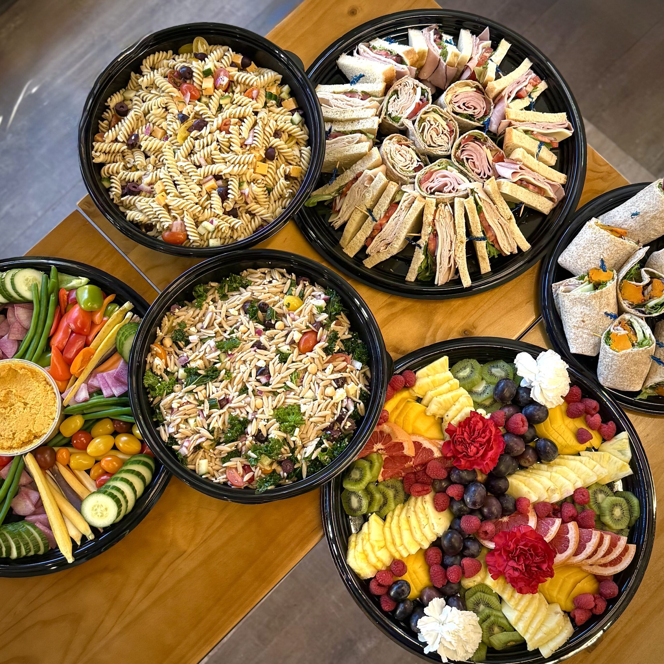 Variety of 6 different catering platters from Prairieland Market that contain everything from wraps and sandwiches to fruits and vegetables.